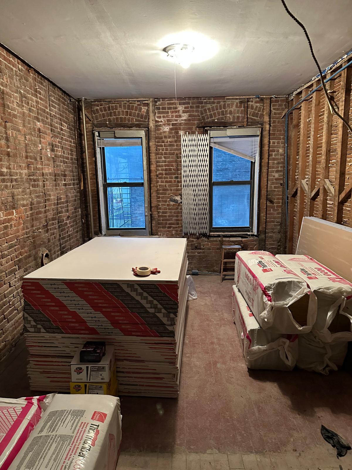 Before: bare room stacked with drywall and insulation